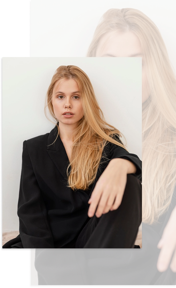 Parlak bir stüdyo ortamında büyük siyah blazer giymiş sarışın bir kadının minimal portresi.