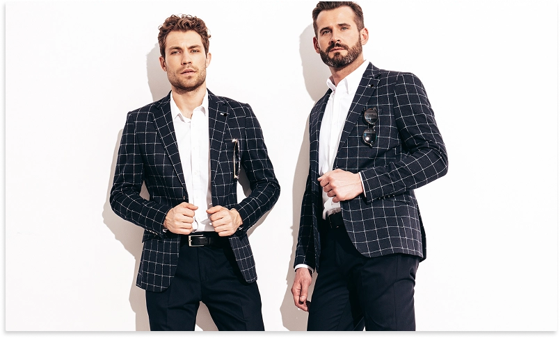 Modern stüdyo çekiminde şık kareli blazer giymiş iki modaya uygun adam poz veriyor.